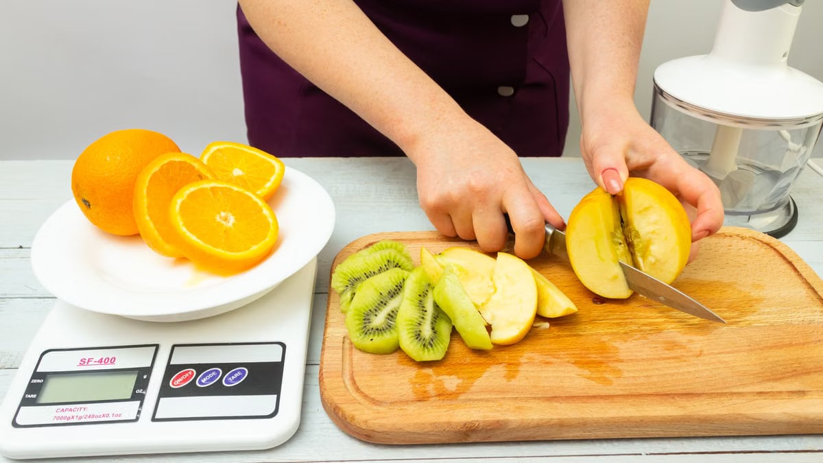 Woman slicing fruits including apple, kiwi, and orange for a healthy meal preparation.